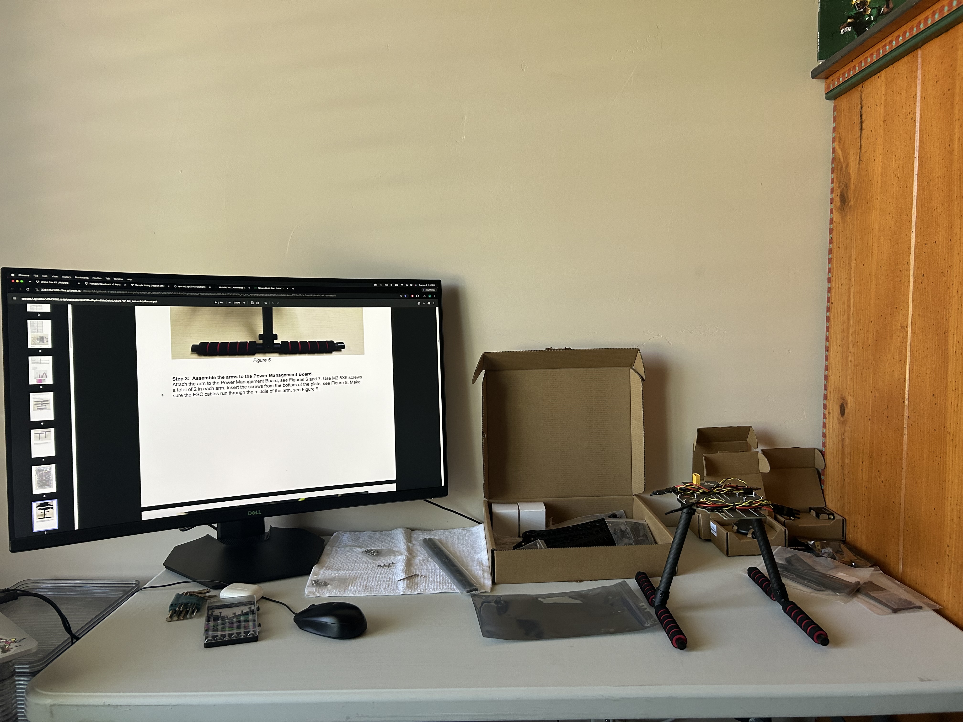 Early Holybro S500 assembly workstation with the manual open on a monitor and frame parts spread across the desk.