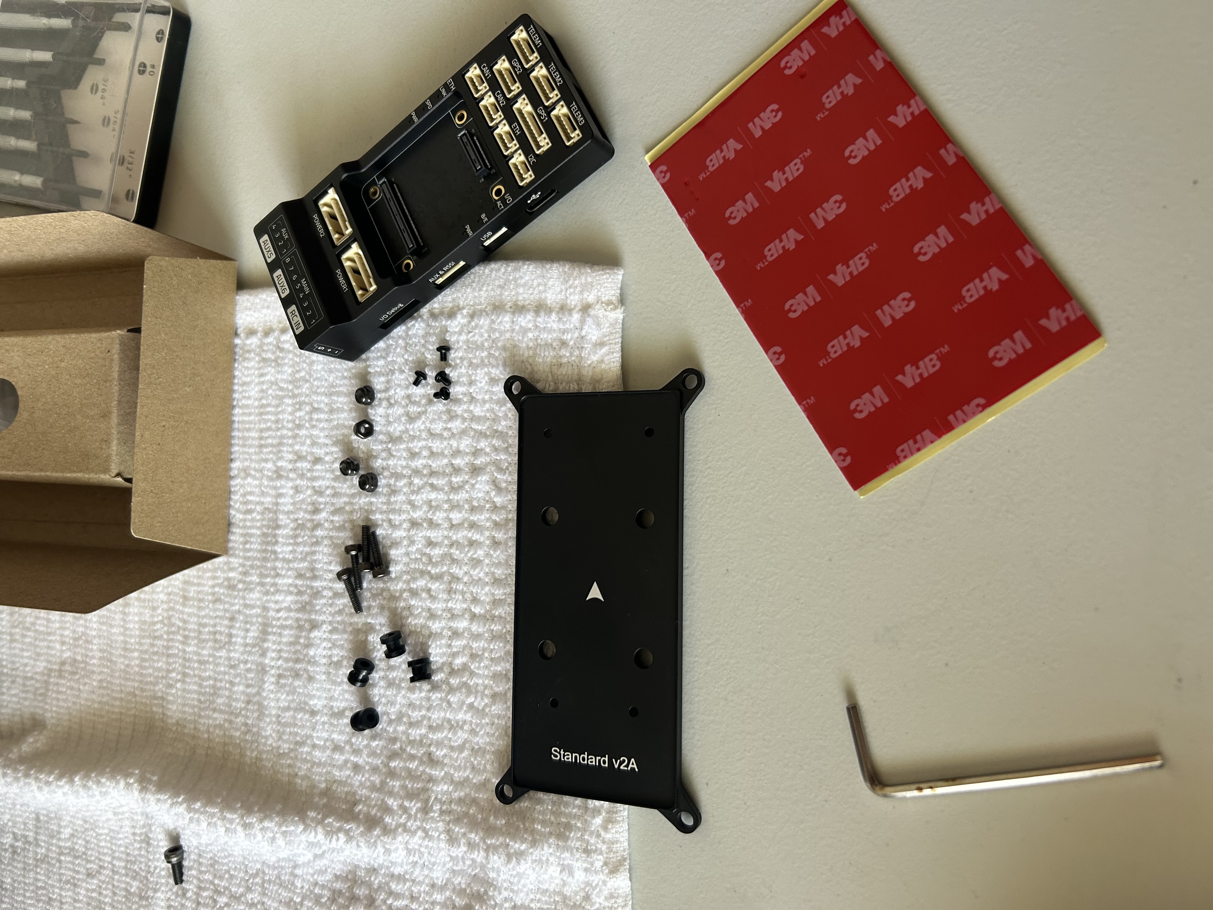 Pixhawk mount plate, screws, vibration components, and adhesive pad laid out on the desk before installation.