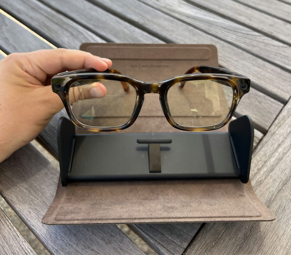 A pair of Meta Glasses held above their open case on an outdoor table